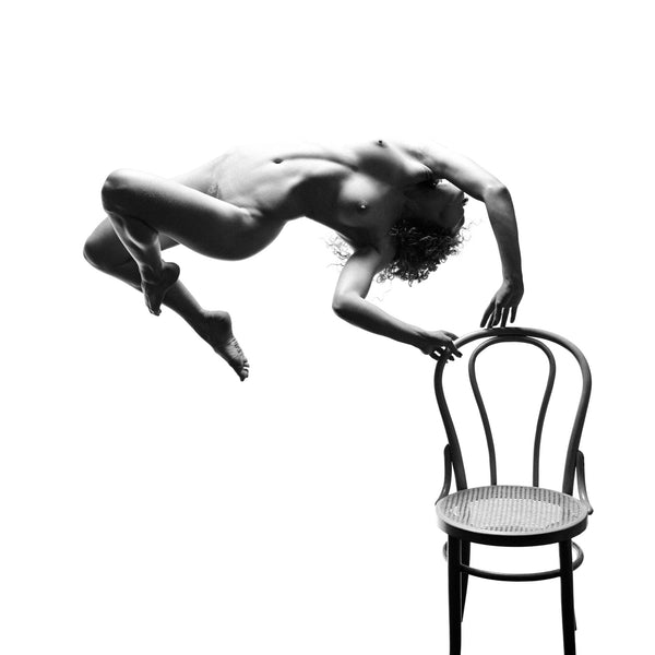 Photography fine art print in black and white. Undressed women levitating, suspended in the air above a classic dinning chair on a white background