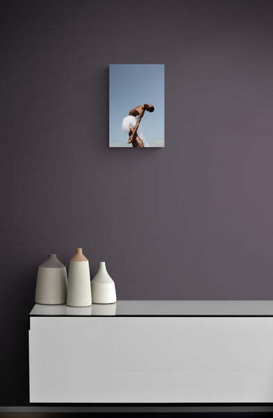 Black male dancer in a meditative movement mood. his skin is glowing into the sun. He is wearing a white skirt on a perfect blue natural sky background. Art print on the wall.