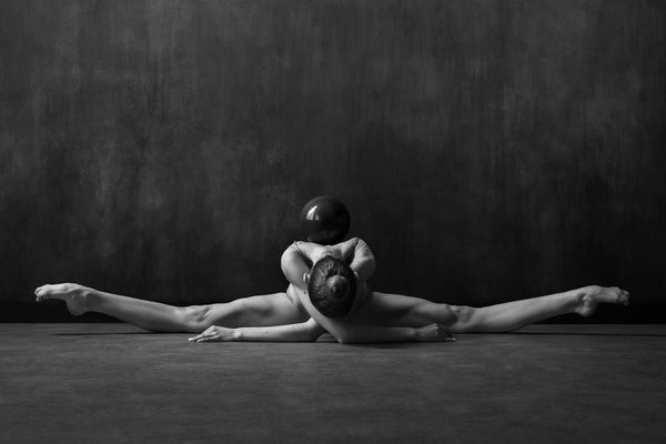Rhythmic gymnastic, stretching on the floor, split, meditation, harmony, black gymnastics ball 'resting' on her back.